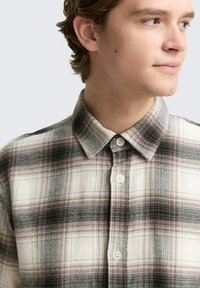 Karierte Hemd in Beige-, Schwarz- und Rottönen. Button-Down-Kragen, vordere Knöpfe, strukturierter Stoff und markantes Karomuster.