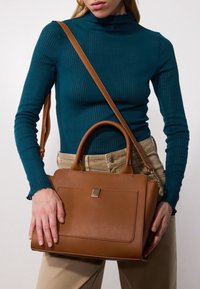 Bolso de cuero marrón con diseño estructurado, dos asas cortas y una correa larga ajustable. Cuenta con un bolsillo delantero con un detalle metálico.