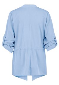 Vaaleansininen, pehmeä kangastoppi, jossa on korkea-matalapituinen helma, rullatut hihat, jotka on kiinnitetty napilla, ja rento istuvuus vyötäröllä.