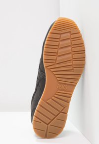 Black athletic shoe sole with textured rubber grips, featuring a gum-colored outer sole and embossed "asics" logo.