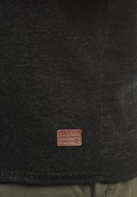 Czarny dzianinowy sweter o teksturowym wykończeniu z brązową skórzaną metką na dole, na której widnieje napis "BLEND GLOBAL JEANMAKER SINCE 1993".