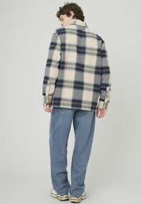 Chemise à carreaux en flanelle crème, marine et grise, avec une coupe droite, des manches longues et des poignets boutonnés, assortie à un jean bleu clair.