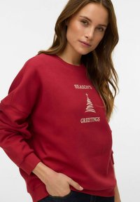 Rdeč pulover s kapuco, na katerem je napis "SEASON'S GREETINGS" in grafika drevesa v bež vezenju. Mehka tkanina z udobnim krojem in obrobljenimi manšetami.