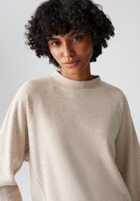 Lichtbeige gebreide trui met een textuurpatroon, hoge hals en een ontspannen pasvorm. Heeft lange mouwen en een zachte, comfortabele stof.