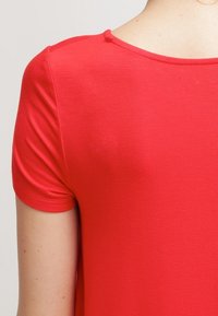 T-shirt rouge à manches courtes avec un col rond, texture lisse et design ajusté. Coutures visibles aux épaules et au cou.