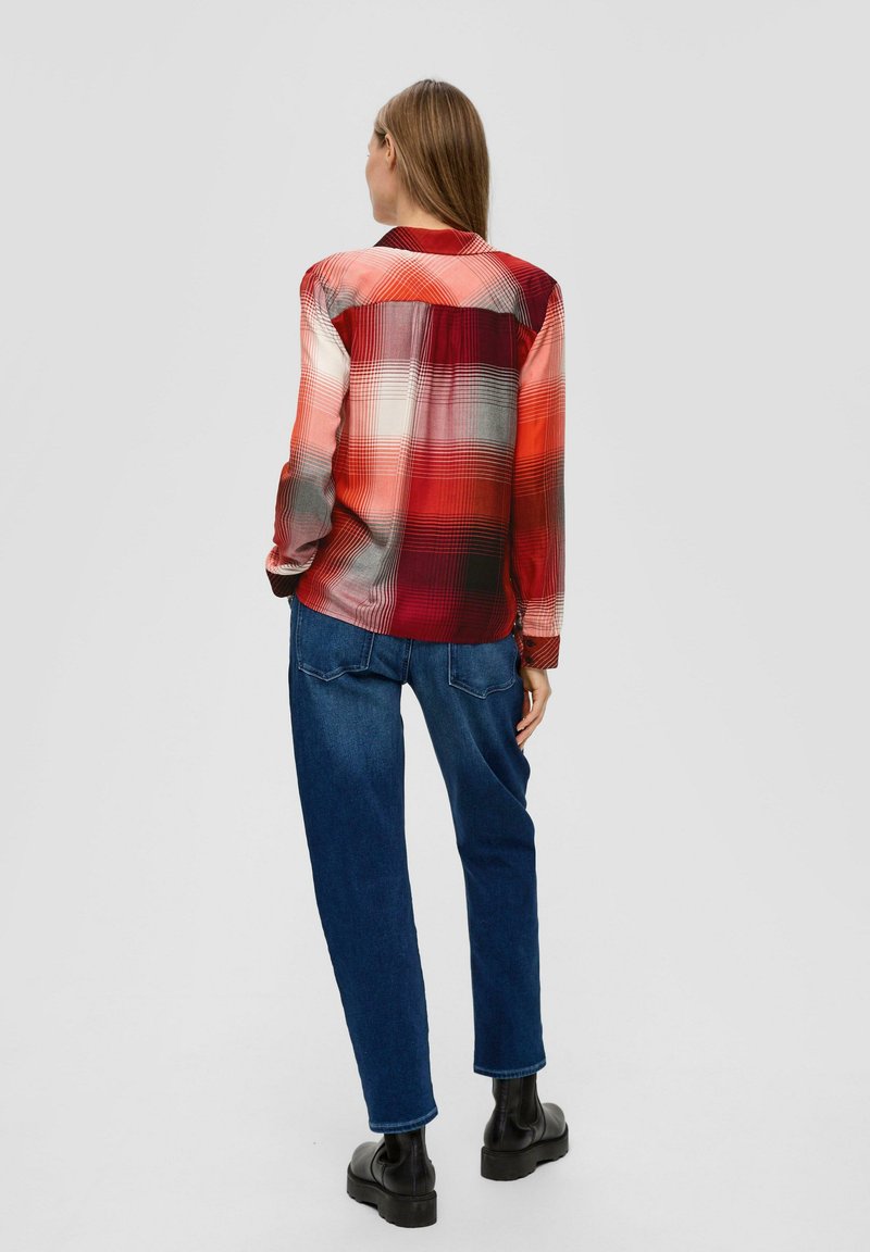 Camicia a quadri rossa e grigia con bottoni e maniche lunghe, indossata con jeans blue a gamba dritta e stivaletti neri alla caviglia. Tessuto morbido.