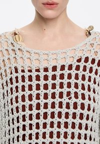 Gehaakte top met een beige patroon en een bruine basis. Heeft een brede halslijn, open weefsel en decoratieve knopen op de schouders.