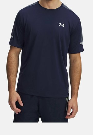 Mężczyzna noszący granatową sportową koszulkę z krótkim rękawem, szarymi panelami na ramionach i białym logo Under Armour na klatce piersiowej.