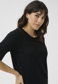 Top in maglia nera con scollatura rotonda e maniche corte. Il tessuto appare morbido e ha una consistenza liscia. Nessun motivo o accessorio notevole.