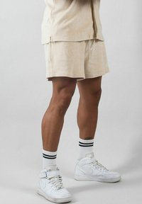 Beige frottéshorts med elastisk midja och dragsko, tillsammans med vita högklackade sneakers och randiga ankelsockor.