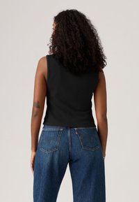 Black ribbed sleeveless top paired with high-waisted blue denim jeans featuring two back pockets with stitching detail.