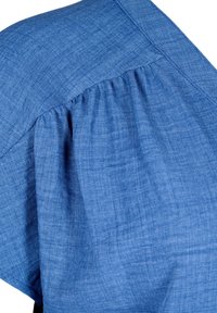 Blå denimtyg med en texturerad yta, som har en samlad ärmdesign och en slät söm längs axeln.