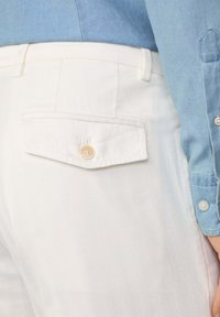 Pantalons en chevrons blancs avec une poche arrière à rabat et un bouton beige, associés à une chemise bleu clair avec un poignet boutonné.
