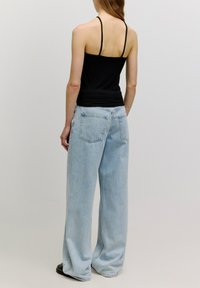 Zwarte geribbelde tanktop met dunne bandjes, gecombineerd met lichtblauwe wijde jeans met achterzakken. Gladde textuur, losse pasvorm.