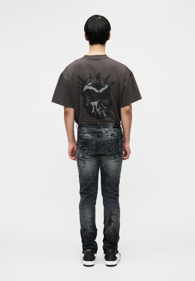 Γκρι φαρδιά μπλούζα με μεγάλο μαύρο γραφικό κρανίο στην πλάτη. Σκούρο, υφασμάτινο τζιν με χαρακτηριστική ξεθώριαση και δύο πίσω τσέπες.