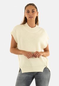 Maglione fine lavorato a maglia color avorio con colletto alto, maniche corte e zip laterali. Presenta una texture a costine e una vestibilità rilassata.