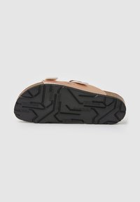 Sandale avec semelle en caoutchouc noire à motifs, brides en cuir marron clair et semelle intérieure en liège, vue par dessous sur fond blanc.