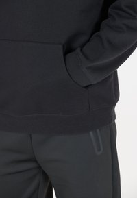 Svart sweatshirt gjord av mjukt tyg med en känguruficka och ribbade manschetter, ihop med skräddarsydda svarta byxor med en stilren sidofickdesign.