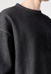 Sweat-shirt à rayures noires avec un col rond côtelé et une texture douce. Présente une coupe décontractée et un léger éclat dans le motif du tissu.