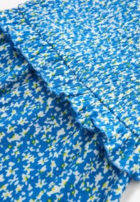 Tissu bleu avec un motif floral en blanc et jaune, présentant un bord froncé, une surface texturée et un design froissé.