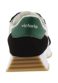 Zapatilla blanca y negra con una lengüeta de talón verde etiquetada como "victoria" y una suela de goma gruesa y texturizada, vista desde atrás.