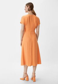 Pomarańczowa sukienka midi z krótkimi rękawami, dopasowanym w talii i zamkiem błyskawicznym z tyłu. W zestawie z dopasowanymi pomarańczowymi szpilkami.