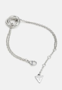 Pulsera de cadena de plata con tres anillos entrelazados, un cierre de langosta y un encanto triangular con la palabra "GUESS" grabada.