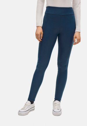 Leggings azul marino con una cinturilla ancha, fabricados con un material elástico. Textura suave, ajuste cónico, combinados con zapatillas blancas.