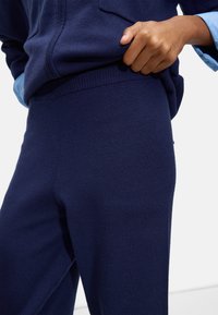 Marineblaue Strick-Sweatpants mit einem gerippten Bund, die eine weiche Textur und eine enganliegende Silhouette aufweisen, teilweise von einer Jacke verdeckt.