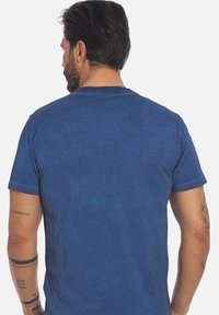 T-shirt in cotone blu con maniche corte, colletto a giro e una texture liscia. Presenta un motivo di tintura sottile e irregolare. Nessun hardware o accento degno di nota.