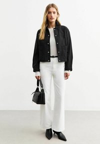Chaqueta negra corta con broches, camiseta blanca de manga larga, pantalones blancos acampanados de cintura alta, tacones negros de punta y un pequeño bolso negro.