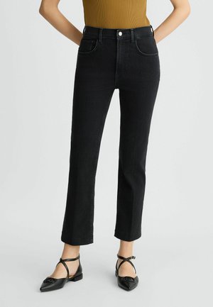 Jeans in denim nero con vita aderente, gamba dritta, dettagli di cucitura sottili e tasche frontali classiche. Indossati con ballerine nere a punta.