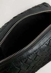 Zwarte geweven leren tas met een rits sluiting. Kenmerkt zich door een metallic rits en een gladde binnenvoering. Compacte en rechthoekige vorm.