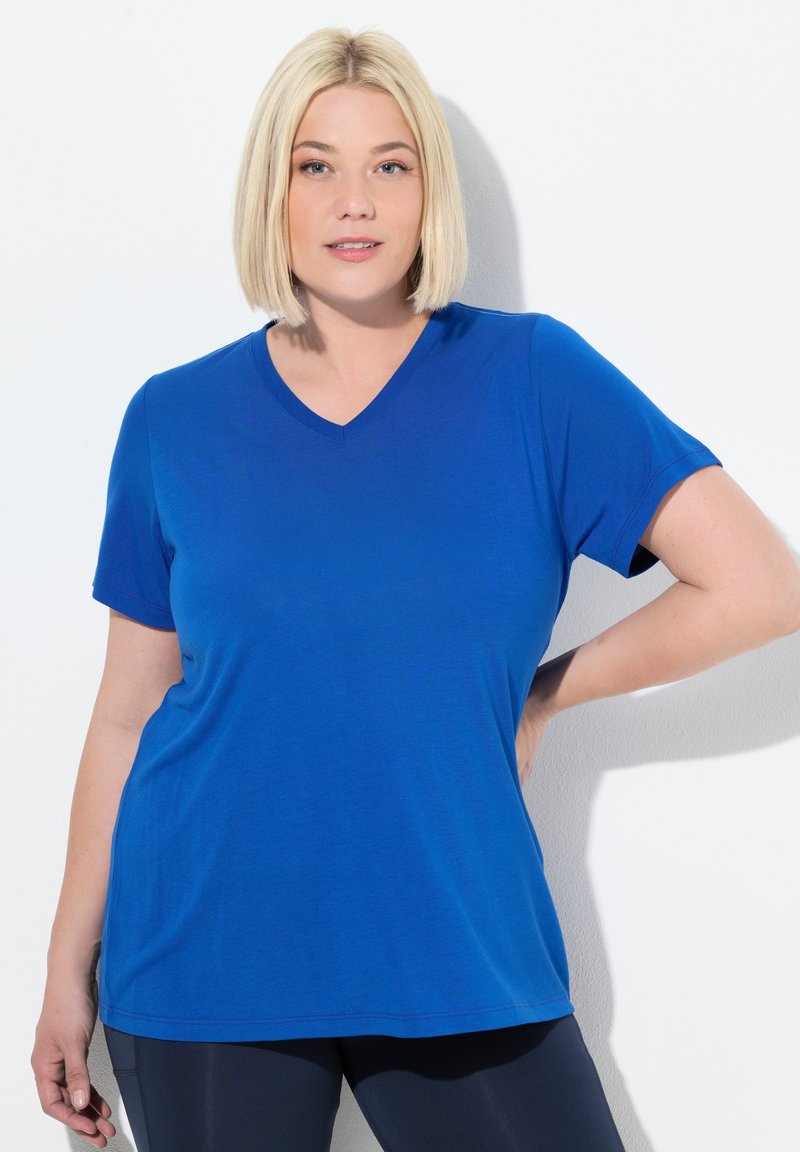 Camiseta de cuello en V azul hecha de material suave, con mangas cortas, que presenta un ajuste relajado y una textura suave, combinada con leggins oscuros.