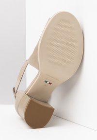 Scarpa con tacco alto beige con tomaia texturizzata, suola liscia e tacco in gomma marrone. Il nome del marchio e la taglia sono stampati sulla suola.