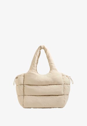 Sac fourre-tout beige rembourré avec un haut arrondi et deux poignées courbes, featuring des panneaux horizontaux cousus et une fermeture à cordon d'un côté.