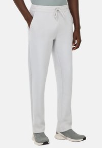 Light grey sweatpants made of soft fabric, featuring side pockets, a drawstring waistband, and tapered legs. Worn with gray athletic shoes.