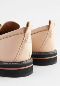 Light pink leather shoes with a sleek design, a textured back, and a contrasting black and rose accent on the sole.