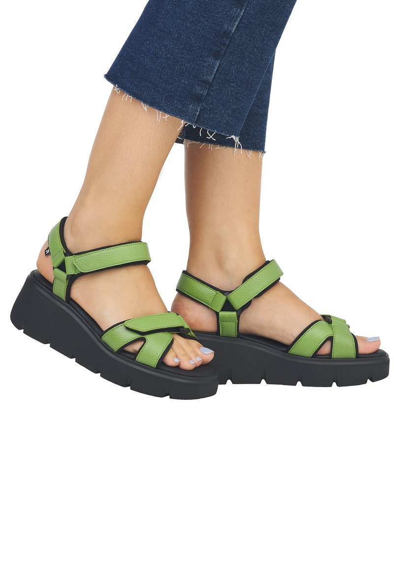 Sandales en cuir vert avec une semelle noire épaisse, présentant plusieurs designs de sangles et des découpes ouvertes à l'avant, offrant un maintien sécurisé.