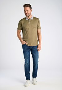 Olivgrön polo t-shirt med en grå krage, med tre knappar. Kombinerad med blå denimjeans och vita sneakers. Enkel, avslappnad design.
