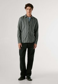 Camicia a quadri verde e nera con colletto, abbinata a jeans neri e scarpe nere. Design semplice, maniche lunghe, vestibilità rilassata.