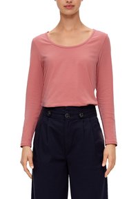 Langärmliges Oberteil in schüchternem Rosa, mit rundem Ausschnitt und weichem, leichtem Stoff; kombiniert mit dunkelgrauen, hochgeschnittenen Hosen mit Knopfdetails.