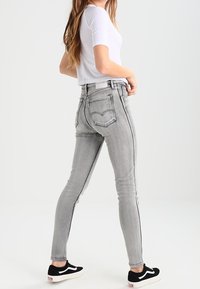 Jeans ajustados gris de cintura alta, con costuras laterales en contraste y bolsillos traseros, combinados con zapatillas negras y una camiseta blanca.