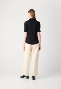 Polo shirt nero a maniche corte, tessuto liscio, orlo arrotondato, abbinato a pantaloni a gamba larga color crema e scarpe nere con tacco a blocco.