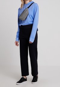 Sudadera con capucha azul de manga larga, pantalones negros de talle alto, zapatillas negras y un bolso cruzado gris con cuadros que aportan contraste y textura al conjunto.