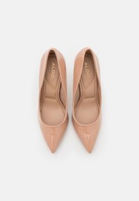 Nude kiilakorkoiset patenttijalkineet, joissa on teräväkärkinen muotoilu ja sileä pinta, minimalistisella designilla ja beige sisävuori.