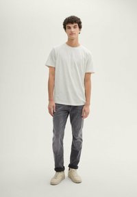 Light gray, short-sleeve t-shirt with a round neckline, paired with dark gray jeans and beige sneakers. Simple, casual design.