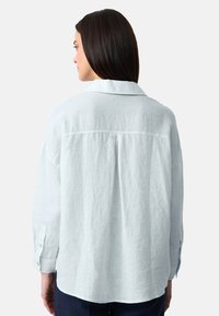 Lichtblauw linnen shirt met een kraag, ontspannen pasvorm en knoopmanchetten. Opvallende rugplooien en een gestructureerde stof.
