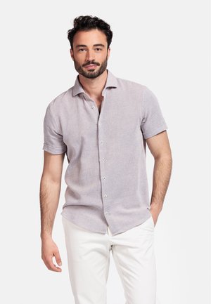 Chemise à manches courtes de couleur claire, à motifs texturés, avec col et boutons blancs, associée à un pantalon blanc.