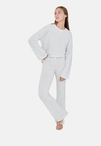 Ensemble de détente rayé en gris clair et blanc. Haut à manches longues avec des poignets larges ; pantalon assorti avec une taille à cordon et des jambes évasées.